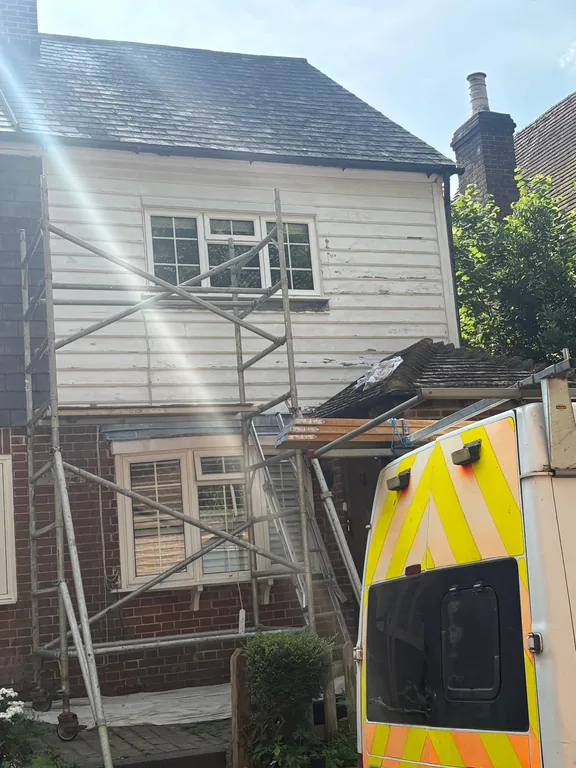 Flaking, weathered paintwork on the weatherboarded upper elevation of a period cottage in Fletching, East Sussex, before restoration