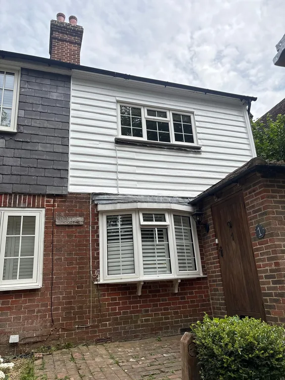 Crisp freshly painted white weatherboards on the completed upper elevation of a period cottage in Fletching, East Sussex