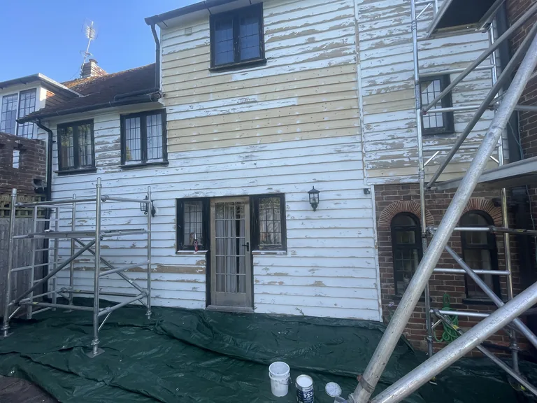 Weatherboarded elevation during preparation, with loose coatings removed and local timber repairs being completed.