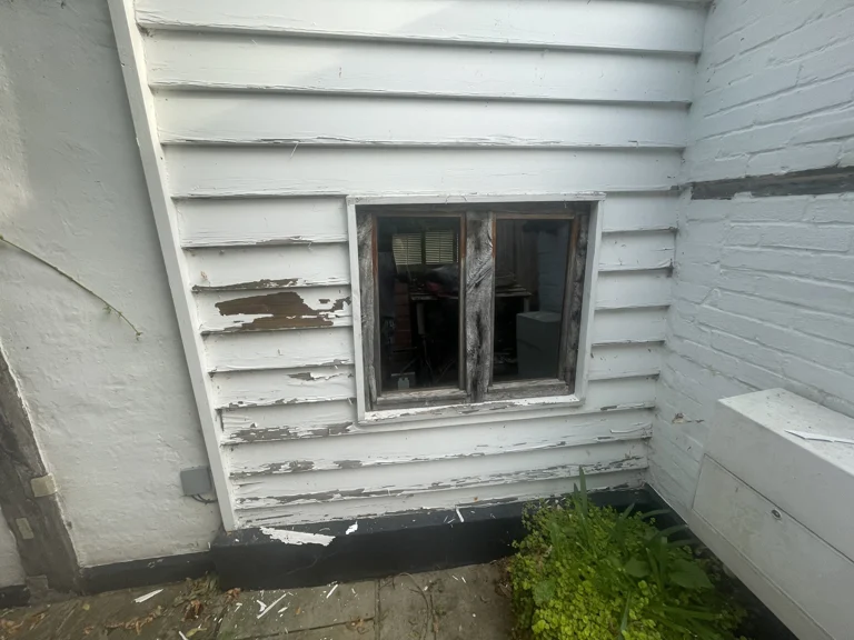 Flaking paint and exposed timber around a window before weatherboard preparation in Boughton Monchelsea
